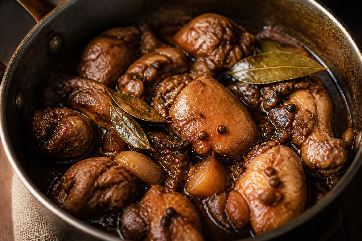 Pot of chicken or pork adobo with vinegar-soy glaze, bay leaves, and peppercorns