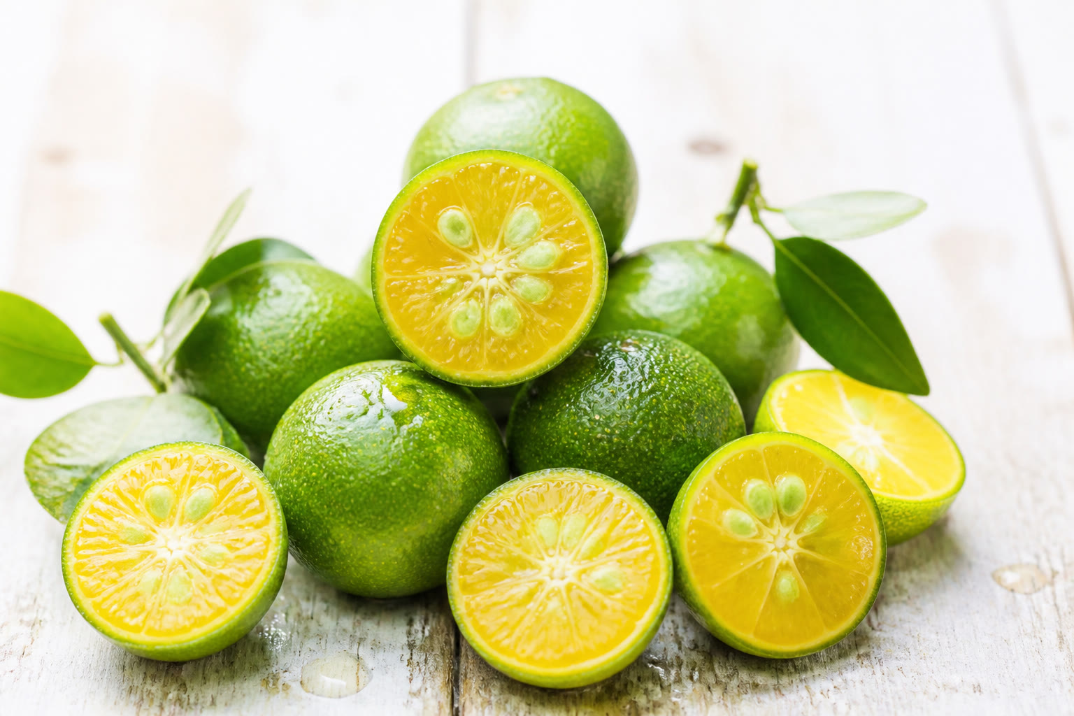 Whole and halved calamansi fruits on a bright wooden surface