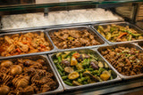 Carenderia glass counter display with trays of Filipino dishes and rice