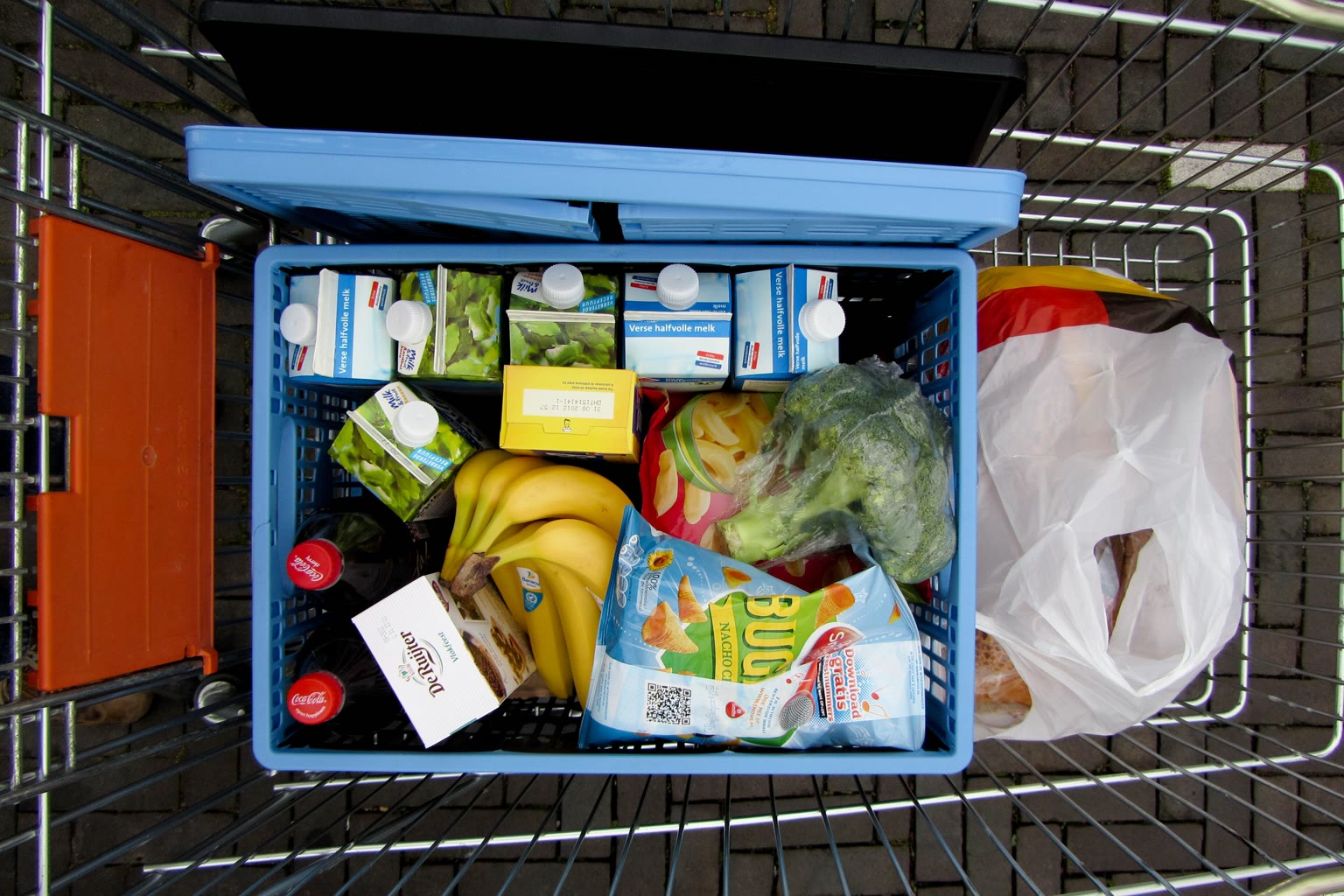 A grocery cart with fresh vegetables, yogurt, legumes, and kimchi viewed from above.
