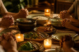 Hands clasped in quiet before a home-cooked meal in warm candlelight