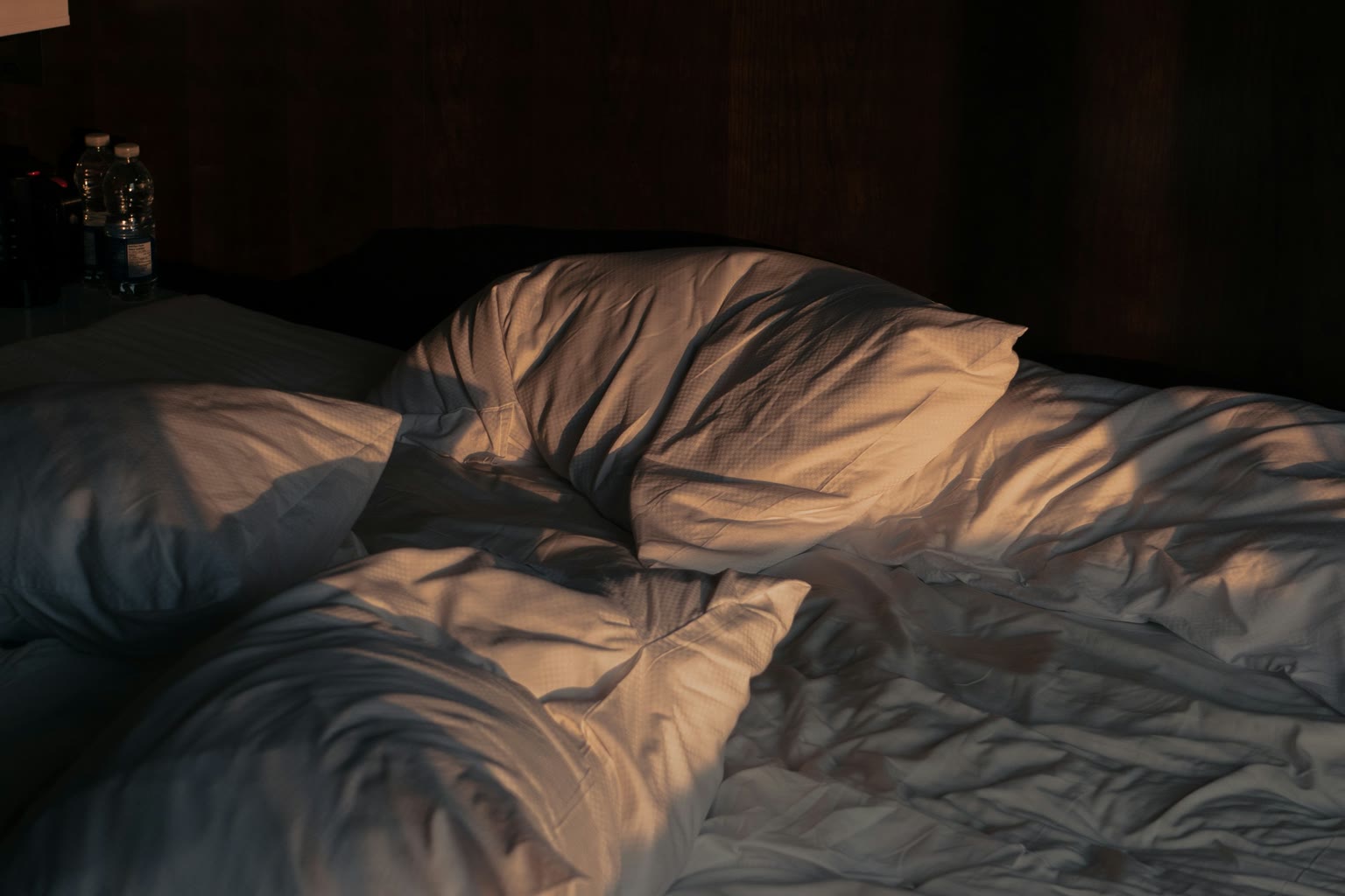 A simple bed with rumpled sheets in soft early morning light.